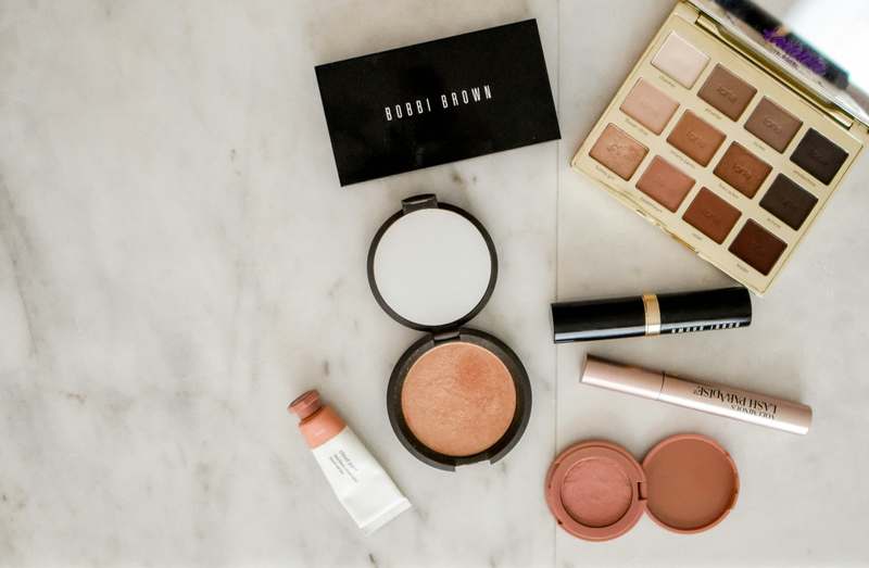 Luxury makeup brushes arranged beside rose gold compacts and a bridal veil on soft pink fabric